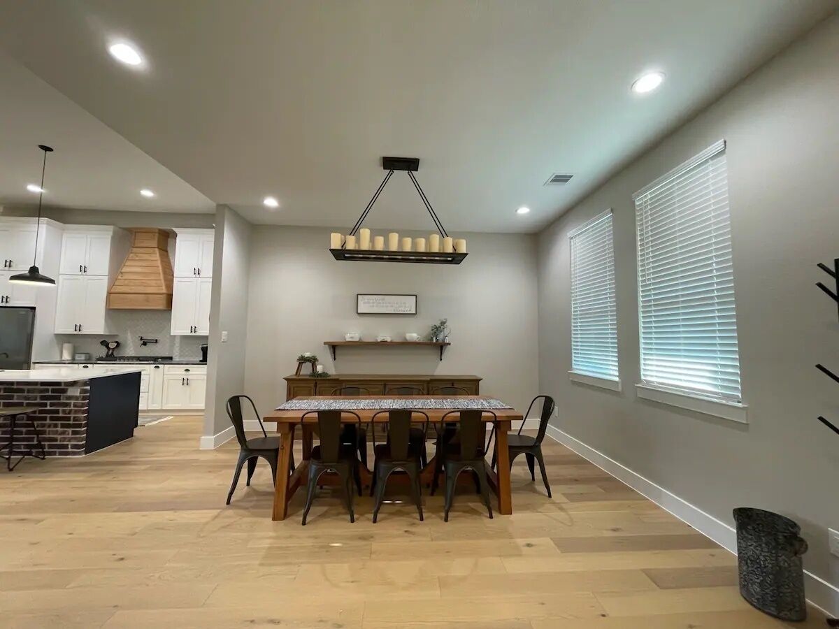 Una cocina moderna con armarios blancos, una isla de madera y una zona de comedor con mesa y sillas.