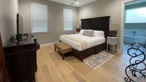 A bedroom with a bed, bedside tables, a desk, a chair, a ceiling fan, and a view of a bathroom.