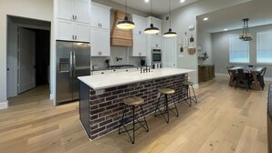 A modern kitchen with white cabinets, a central island with stools, and pendant lighting.