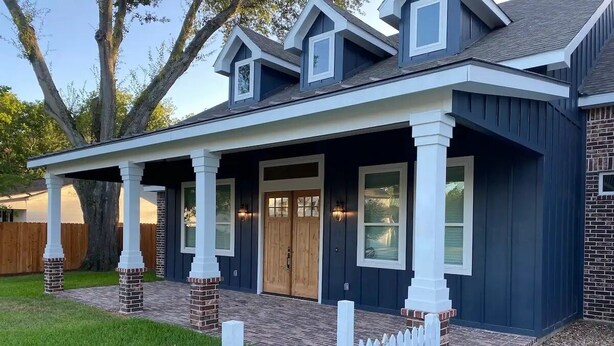 A residential house with a covered porch, brick pillars, and a white picket fence.