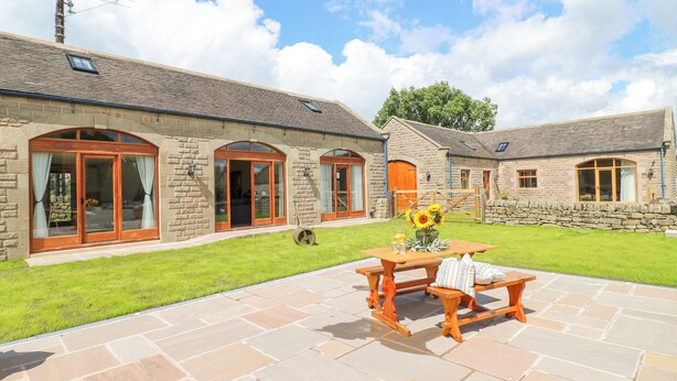A stone building with large windows and a patio area with a table and benches. - Brightside (Matlock)