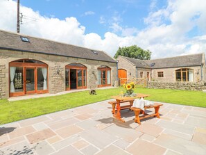 A stone building with large windows and a patio area with a table and benches. - Brightside (Matlock)