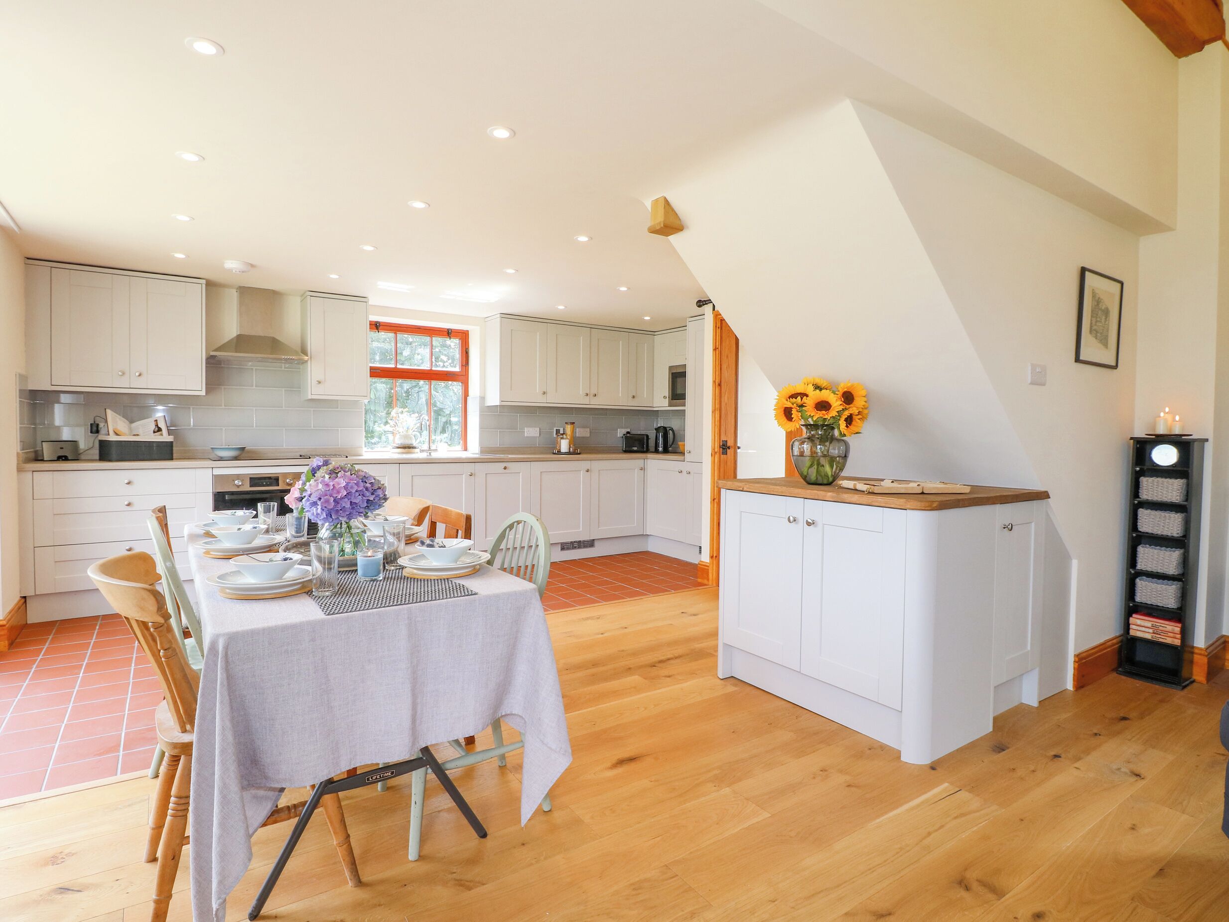 A spacious kitchen with white cabinets, a dining table set for four, and a small island with a vase of sunflowers.