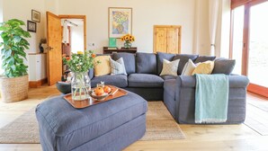A modern living room with a grey sectional sofa, wooden beams on the ceiling, a large window, and a potted plant. - Brightside (Matlock)