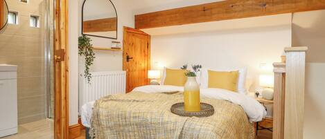 A bedroom with a wooden ceiling, a bed with white bedding, a bedside table with a lamp, and a small plant on the wall.