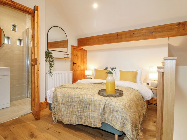 Ein Schlafzimmer mit Holzboden, einem Bett mit weißer Bettwäsche, einem Nachttisch mit Lampe und einer kleinen Pflanze an der Wand.