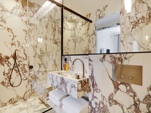 Bathroom features a large mirror, two sinks, and a glass shower enclosure with a handheld showerhead.