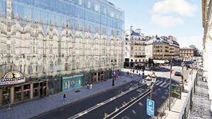 Un edificio moderno con fachada de vidrio, escaparate visible con señalización y una calle con peatones.