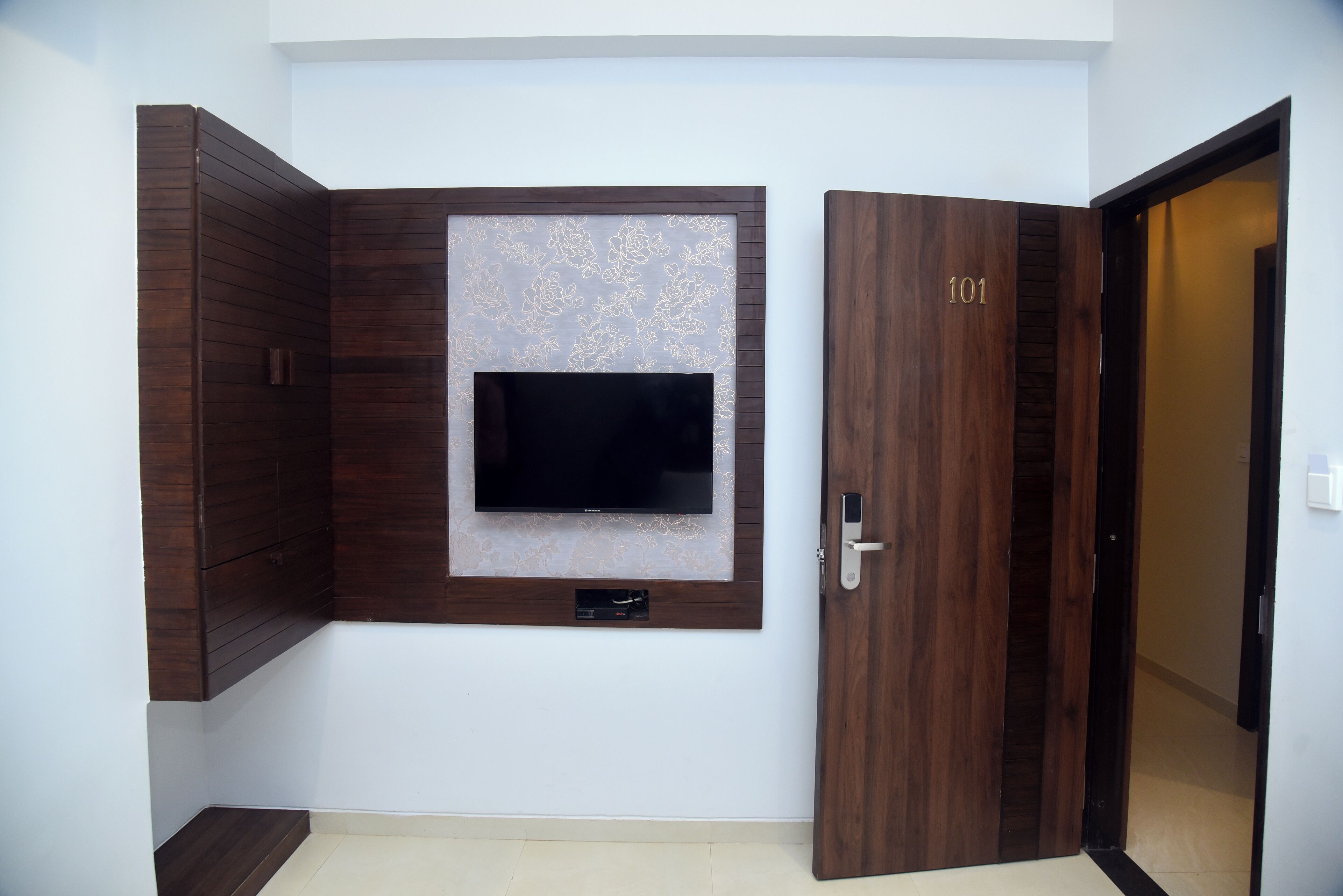 A room with a dark wooden wardrobe, a mounted television, and a door labeled '101'.