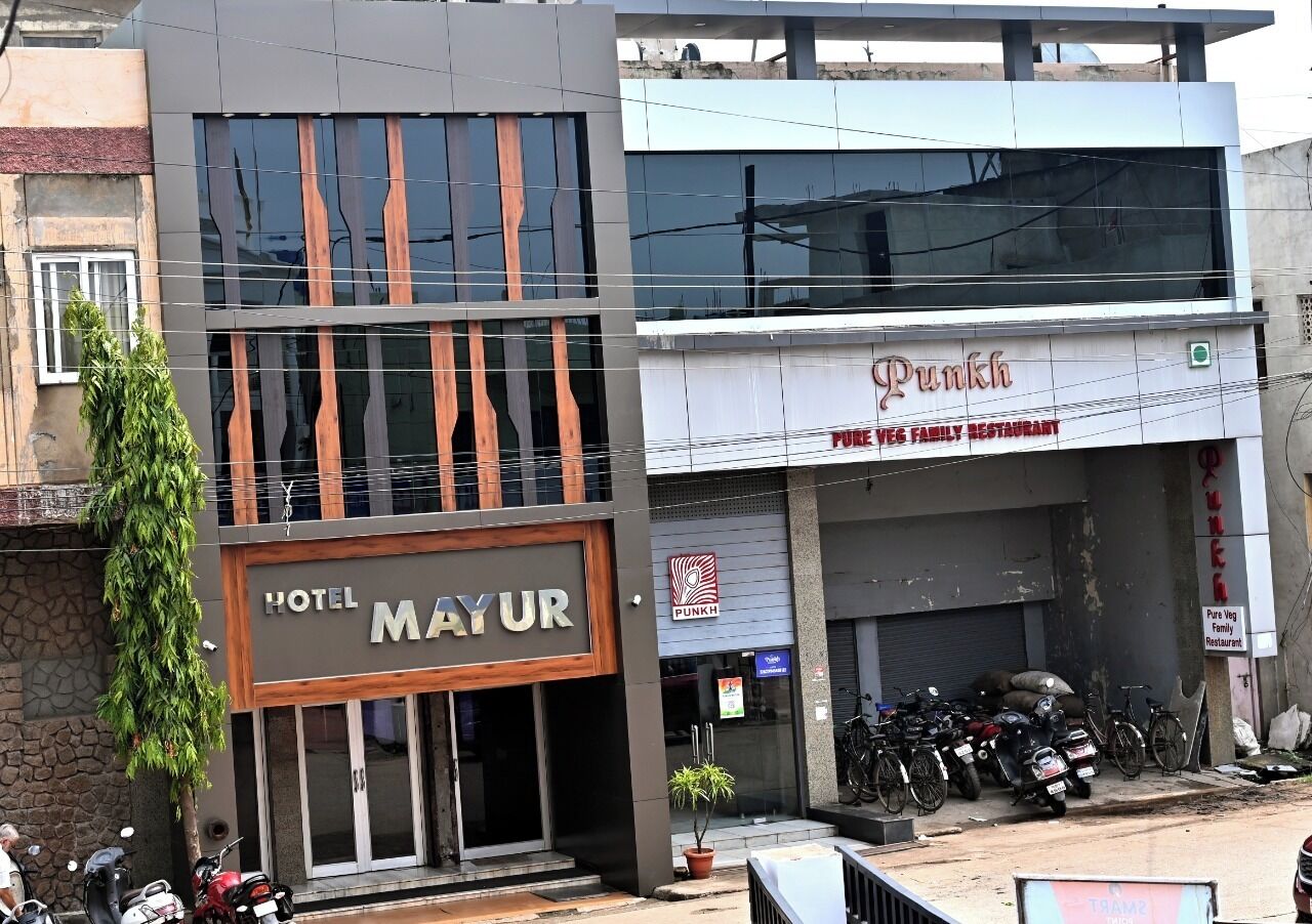 A building with a 'HOTEL MAYUR' sign, a 'Punkh' restaurant, and several parked motorcycles.