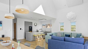 A modern living space with a blue sofa, wooden dining table, and a kitchen area. - 4 The Vista, Willingcott Nr Woolacombe - Outdoor shower/ On-site pool / EV charger/ Ecohome (Woolacombe)