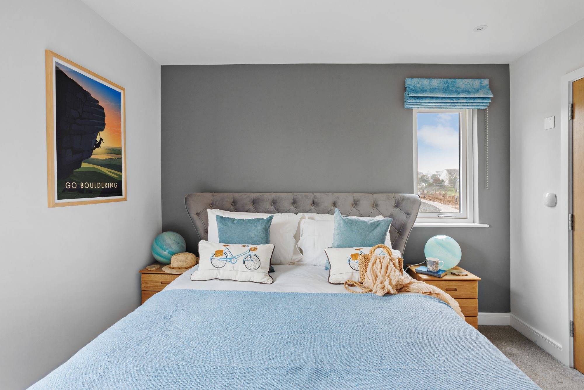 A bedroom with a large bed, a nightstand, a window with blue curtains, and a poster on the wall.