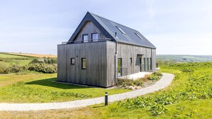 A modern wooden house with a sloped roof, a gravel path leading to the entrance, and a scenic countryside view. - 4 The Vista, Willingcott Nr Woolacombe - Outdoor shower/ On-site pool / EV charger/ Ecohome (Woolacombe)