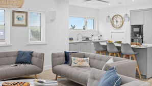 A modern living room with grey sofas, a dining area, and a kitchen with white cabinets. - 7 The Vista - Hot tub - Pet friendly - On-site pool - EV Charger - Ecohome (Woolacombe)