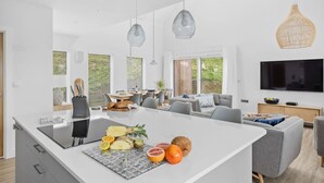 A modern kitchen with a central island, dining area, and a living space with a flat-screen TV. - 7 The Vista - Hot tub - Pet friendly - On-site pool - EV Charger - Ecohome (Woolacombe)