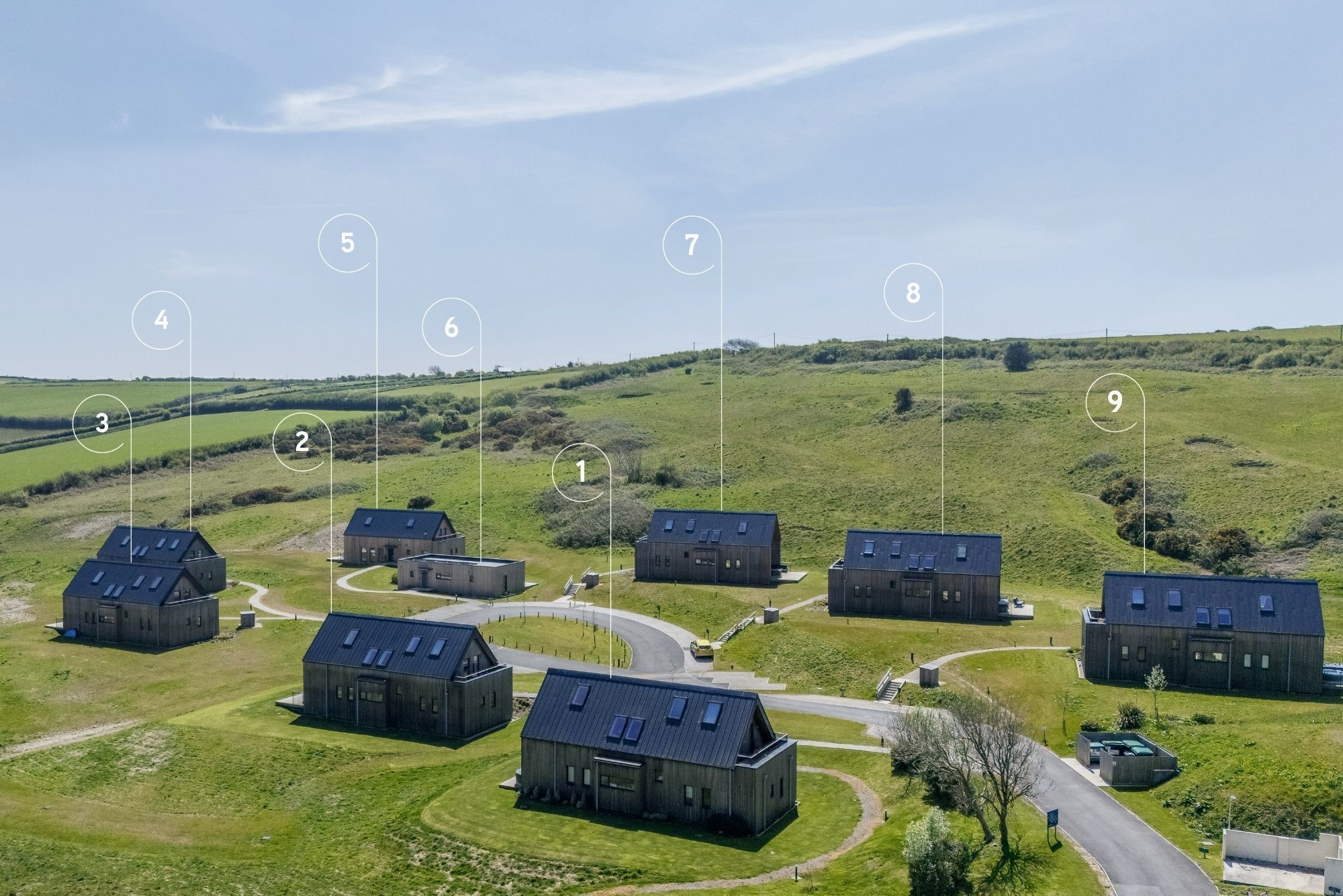 An aerial view of a rural property with multiple buildings numbered 1-9, surrounded by green fields and a clear sky.