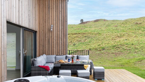 A wooden deck with outdoor furniture, a hot tub, and a scenic hillside view. - 7 The Vista - Hot tub - Pet friendly - On-site pool - EV Charger - Ecohome (Woolacombe)