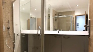 Ein modernes Badezimmer mit einer Duschkabine aus Glas, einem großen Spiegel und einem dunklen Waschtisch.
