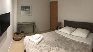 Ein Schlafzimmer mit einem Bett, einem Schreibtisch, einem Sessel, einem Fernseher und einem Kleiderschrank.