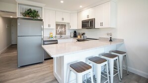 Una cocina moderna con armarios blancos, una isla central con taburetes, un refrigerador y un microondas.