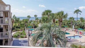 Un resort con piscina rodeada de palmeras y vista al océano.