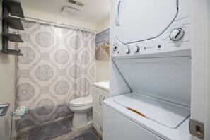 Une salle de bain avec un rideau de douche à motifs, des toilettes et un appareil combiné lave-linge et sèche-linge.