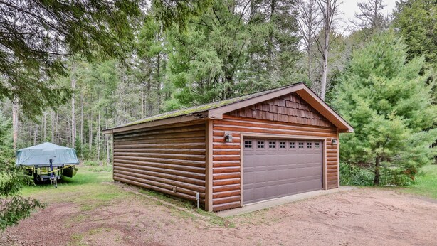 A wooden cabin with a garage, surrounded by dense forest. - Stepaway Vacation Rentals - Hemlock House on Little St. Germain (St. Germain)