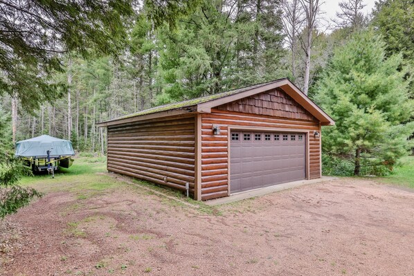 A wooden cabin with a garage, surrounded by dense forest. - Stepaway Vacation Rentals - Hemlock House on Little St. Germain (St. Germain)