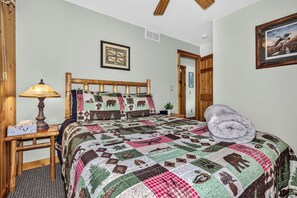 A bedroom with a wooden headboard, a quilt with animal patterns, a bedside lamp, and a framed picture on the wall. - Stepaway Vacation Rentals - Hemlock House on Little St. Germain (St. Germain)