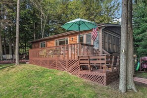 A wooden cabin with a deck, a staircase, and an American flag. - Stepaway Vacation Rentals - Hemlock House on Little St. Germain (St. Germain)