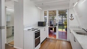 Cozinha compacta com fogão, forno e micro-ondas embutidos, bancada pequena e porta de vidro deslizante para uma área de pátio.
