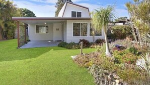 Uma casa térrea com varanda frontal, um pequeno jardim e céu limpo.