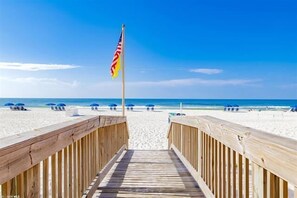 A wooden boardwalk leading to a beach with umbrellas and a flag.