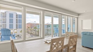 Un coin repas avec une table et des chaises, de grandes fenêtres donnant sur des immeubles et une chaise bleue à l’extérieur.