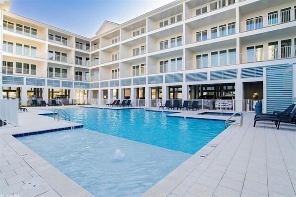 A multi-story hotel with a central swimming pool, balconies, and outdoor seating areas.