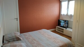 Un dormitorio con cama, televisor y ventana con cortinas.
