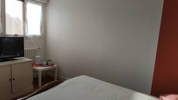 Ein Hotelzimmer mit einem Bett, einem Fernseher auf einem Schreibtisch, einem Sessel und einem Fenster mit Vorhängen.