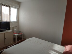 Una habitación de hotel con cama, televisión sobre un escritorio, una silla y una ventana con cortinas.