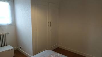 A bedroom with a bed, a wardrobe, a radiator, and a window.