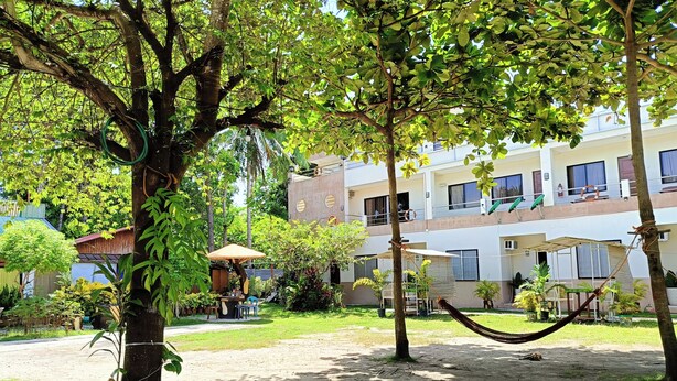 Un patio con una hamaca, árboles y un edificio con balcones.