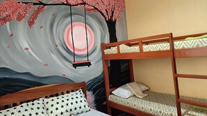 Una habitación con literas, una cama con un cojín estampado con estrellas, y un mural de un árbol con hojas rosadas y un diseño circular.