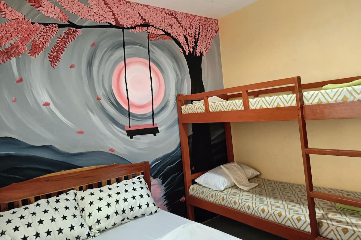 Une chambre avec des lits superposés, un lit orné d’un oreiller à motifs d’étoiles et une fresque représentant un arbre aux feuilles roses et un motif circulaire.