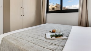 Un dormitori amb llit, finestra i vista d'edificis a l'exterior.