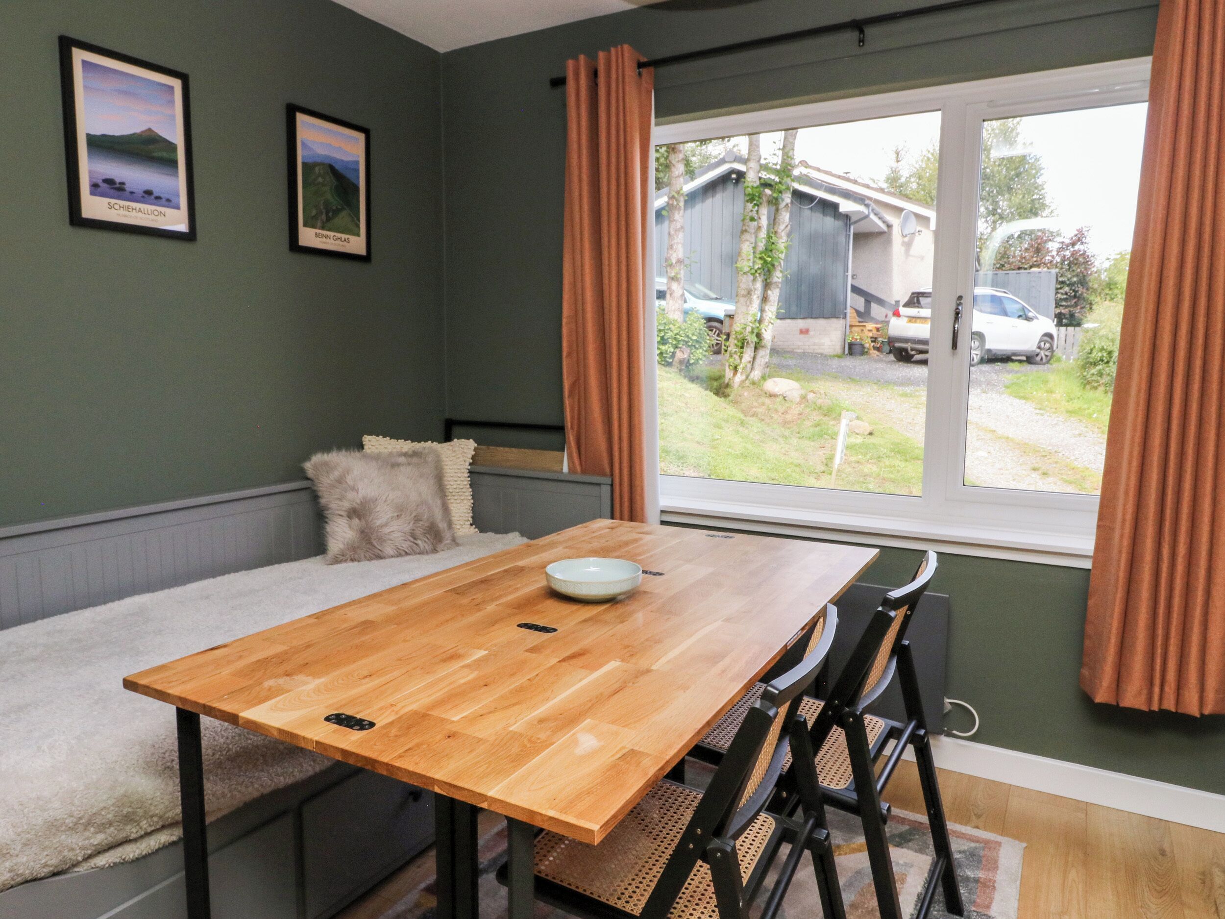 Una habitación con una mesa de madera, dos sillas, un banco y una ventana con cortinas.