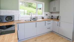 Una cocina moderna con armarios blancos, encimera de madera, microondas integrado, fregadero y ventana con vistas al verdor.