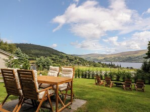 A patio with wooden chairs and a table, overlooking a scenic landscape with hills and a lake. - Beech Cottage (Aberfeldy)