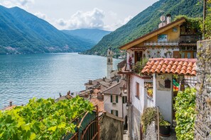 A coastal building with a bell tower, terracotta roof tiles, and a view of a lake and mountains. - Casa Veligato 2 (San Siro)