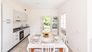 A modern kitchen with white cabinetry, a dining table set for six, and a view of a garden through an open door. - Casa Veligato 2 (San Siro)