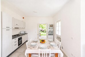A modern kitchen with white cabinetry, a dining table set for six, and a view of a garden through an open door. - Casa Veligato 2 (San Siro)