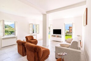 A spacious living room with a large TV, two brown sofas, a grey sofa, and a small table with a tray.
